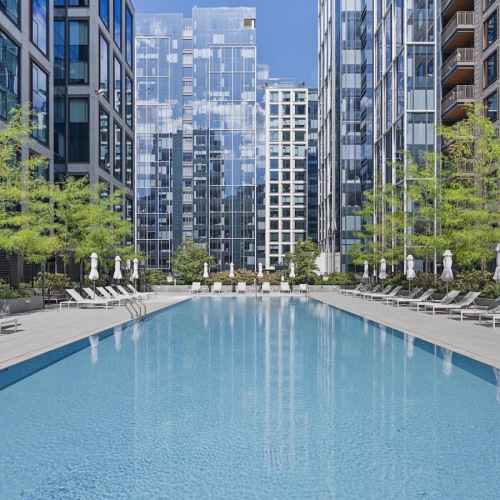 Swimming Pool The pool area at The Alyx at Echelon Seaport in Boston, featuring lounge chairs, umbrellas, and a view of the apartments.