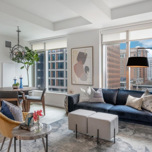 Spacious and well-lit living spaces Model living room at our apartments for rent in Boston, MA, featuring wood grain floor paneling and a dining room table.