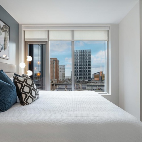 Beautiful bedrooms to fit every need Model bedroom at our apartments for rent in Boston, MA, featuring white bedspread and a view of Downtown Boston.