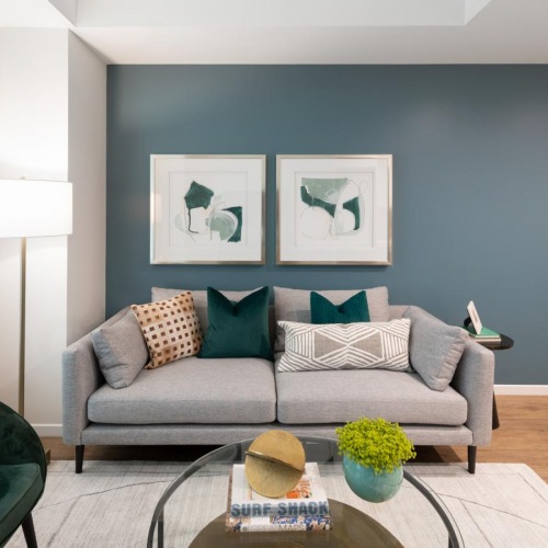 Beautiful living areas to match your lifestyle Model living room at our apartments for rent in Boston, MA, featuring wood grain floor paneling and a grey couch.